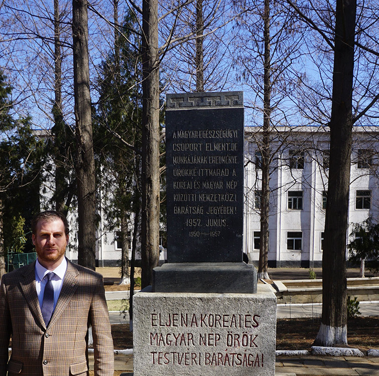 Dr. Csoma Mózes nagykövet Észak-Koreában, az egykori magyar kórház udvarán lévő kétnyelvű emlékoszlop előtt, melyet 1957-ben a távozó magyar orvosok állítottak munkájuk mementójaként